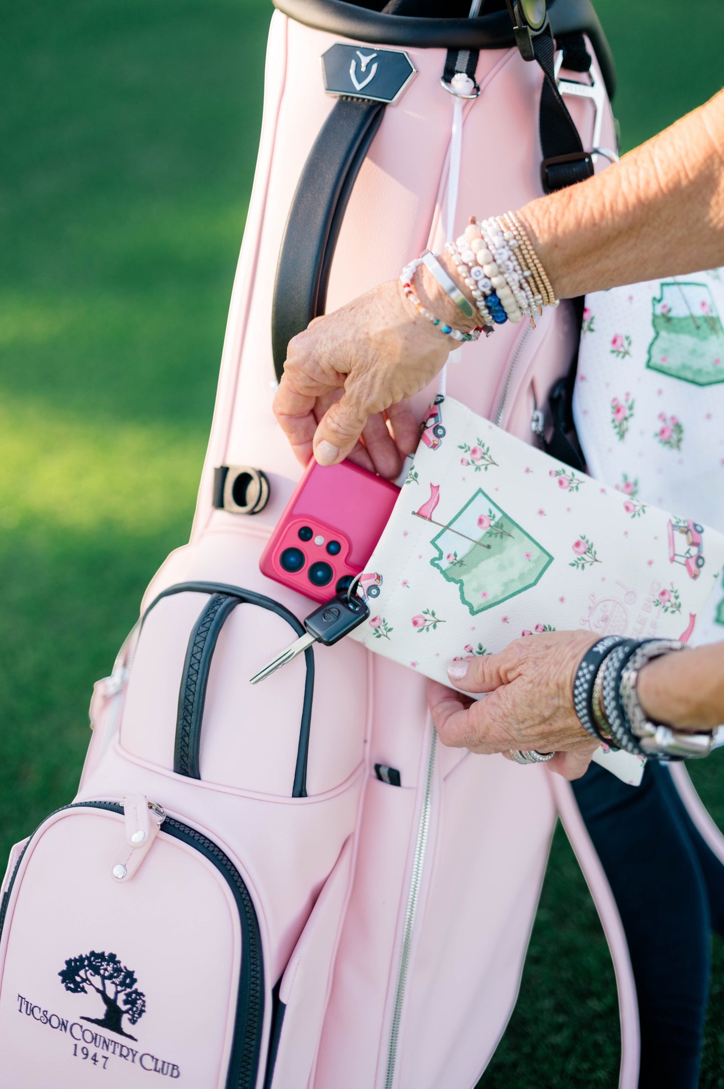 Snuggle Bug Golf Arizona Bloom drawstring pouch with floral print held against a light pink golf bag on a course.