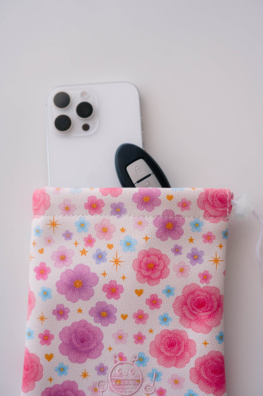 Snuggle Bug Golf Starlight Bloom drawstring pouch with pink floral print, holding a smartphone and car key.