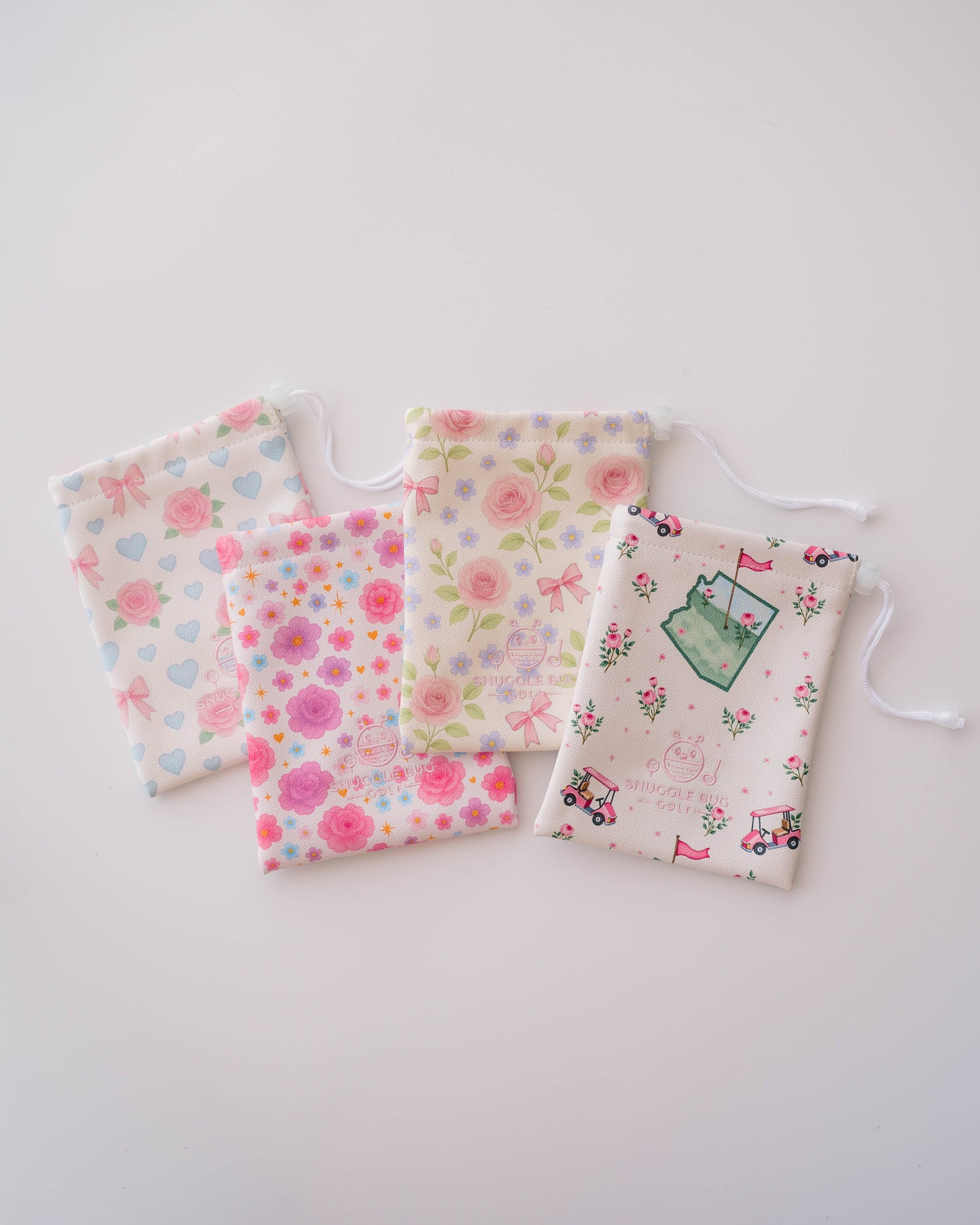 Snuggle Bug Golf drawstring pouches featuring pink floral, daisy, star, heart, and golf cart patterns on eco-leather.