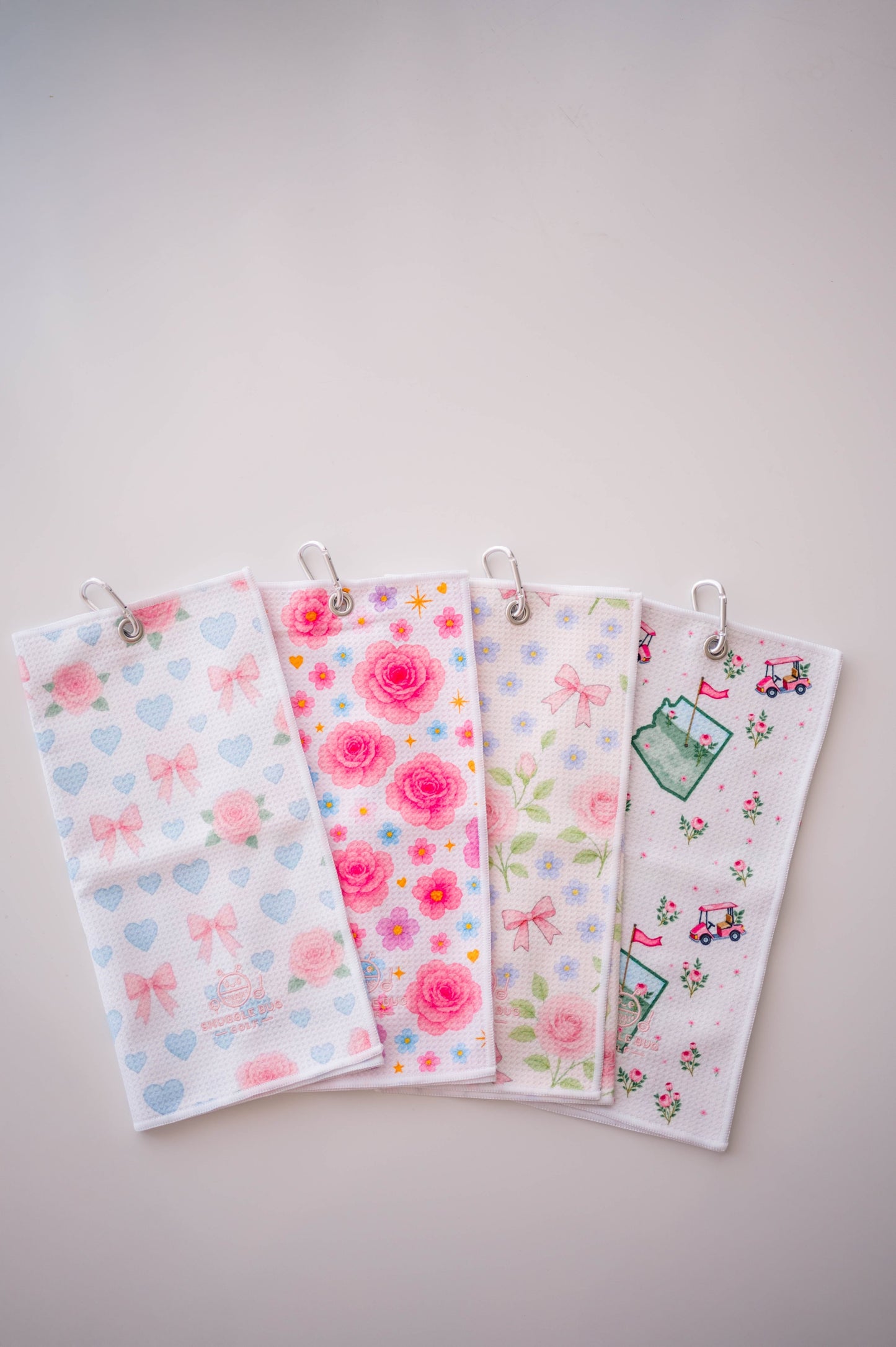 Snuggle Bug Golf microfiber golf towels featuring floral, heart, and bow patterns with silver grommet clips.