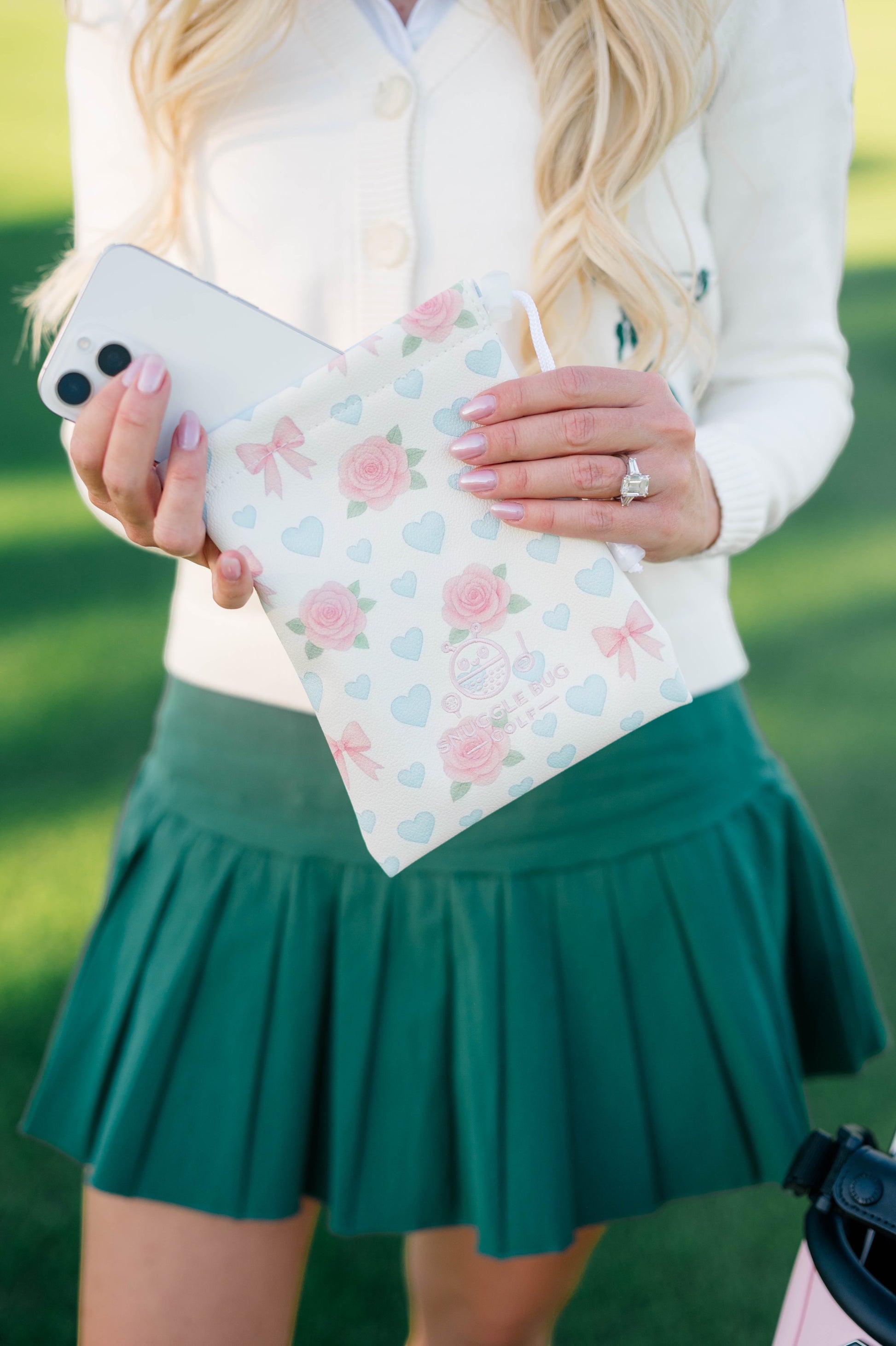 Snuggle Bug Golf drawstring pouch in blush with pink roses, blue hearts, and bows, held by a woman on a golf course.