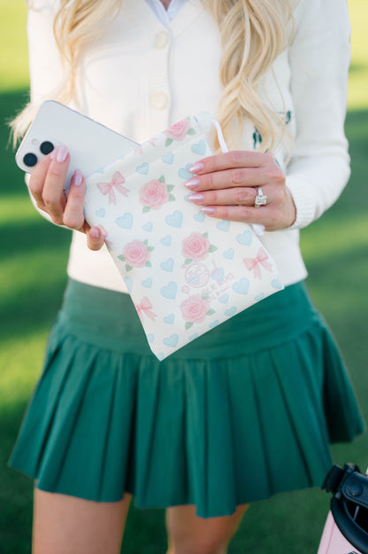 Snuggle Bug Golf drawstring pouch in blush with pink roses, blue hearts, and bows, held by a woman on a golf course.
