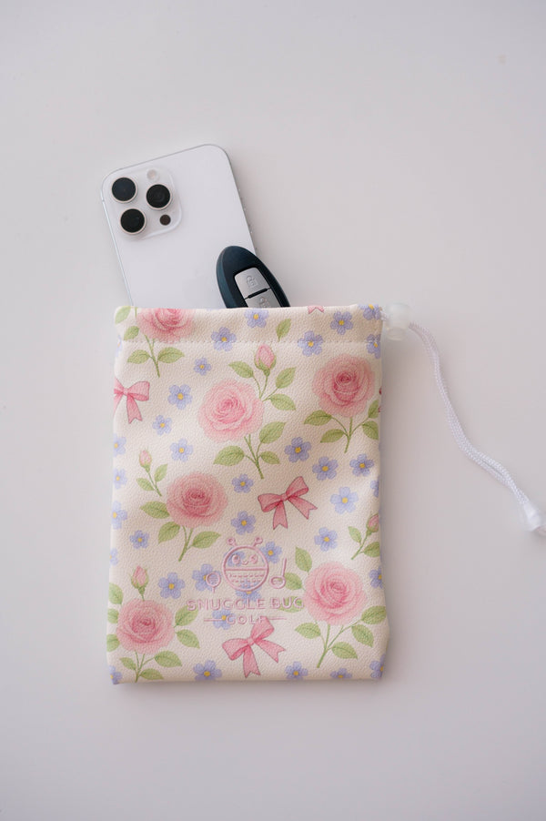 Snuggle Bug Golf Whisper Rose drawstring pouch with floral print, holding a smartphone and car key on white surface.