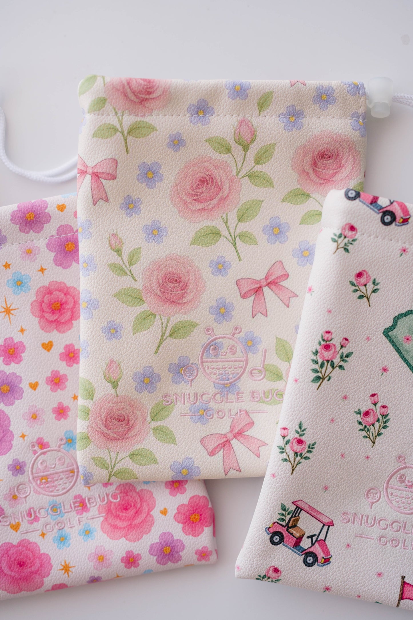 Snuggle Bug Golf Whisper Rose drawstring pouches in cream eco-leather with floral, bow, and golf cart patterns.