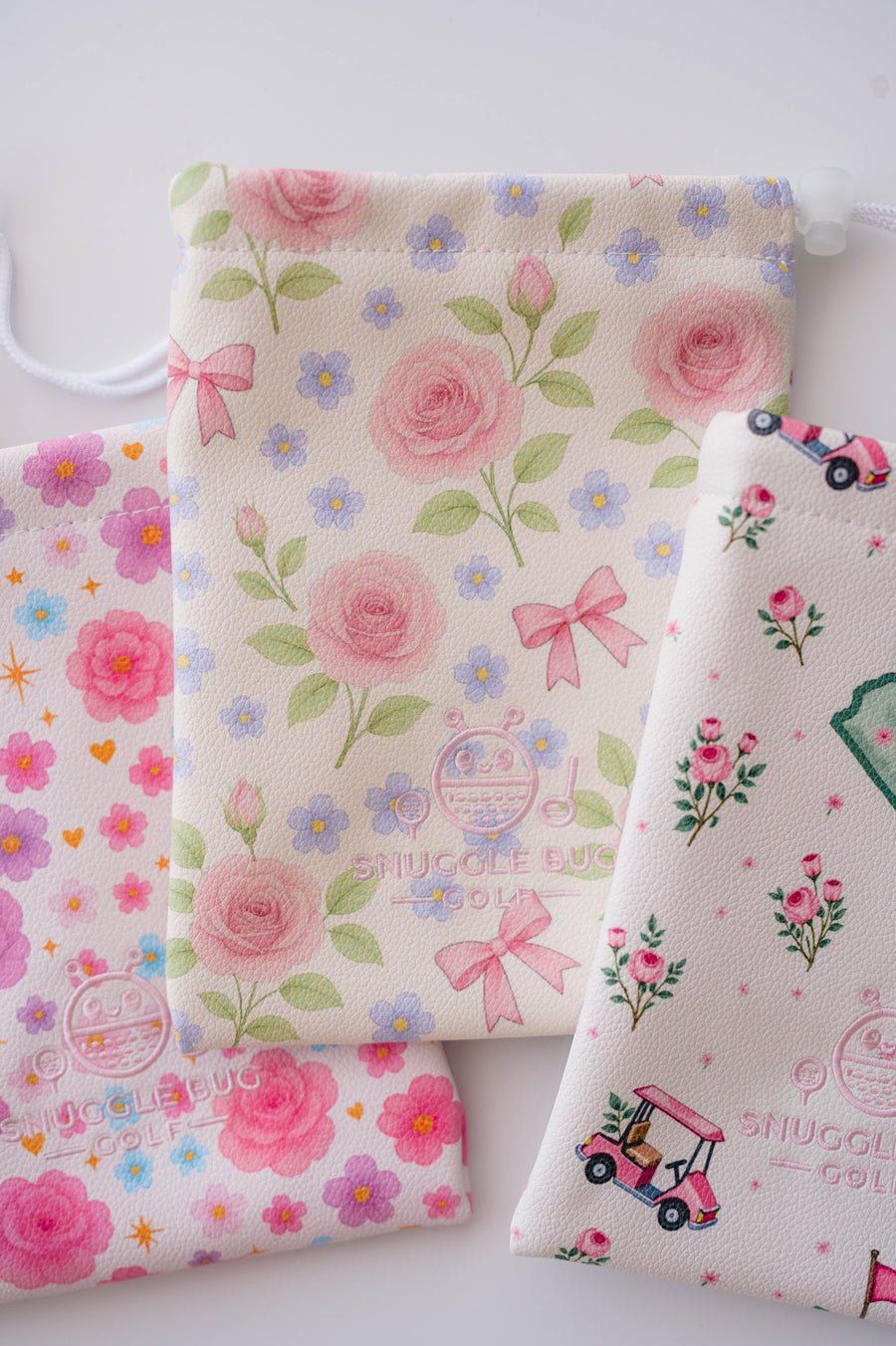 Snuggle Bug Golf Whisper Rose drawstring pouches in cream eco-leather with floral, bow, and golf cart patterns.